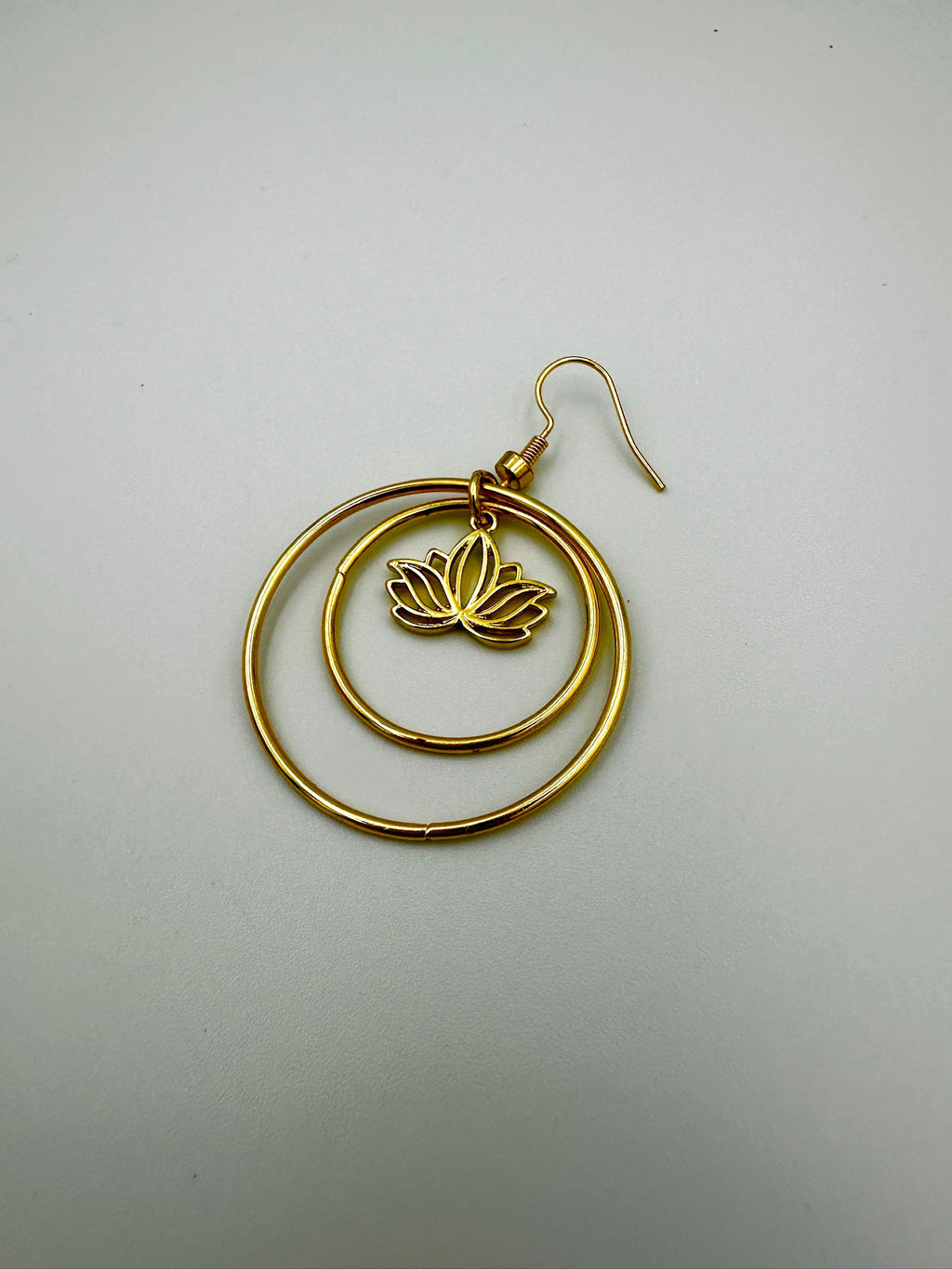 Gold hoop earring with a lotus flower design on a light gray background