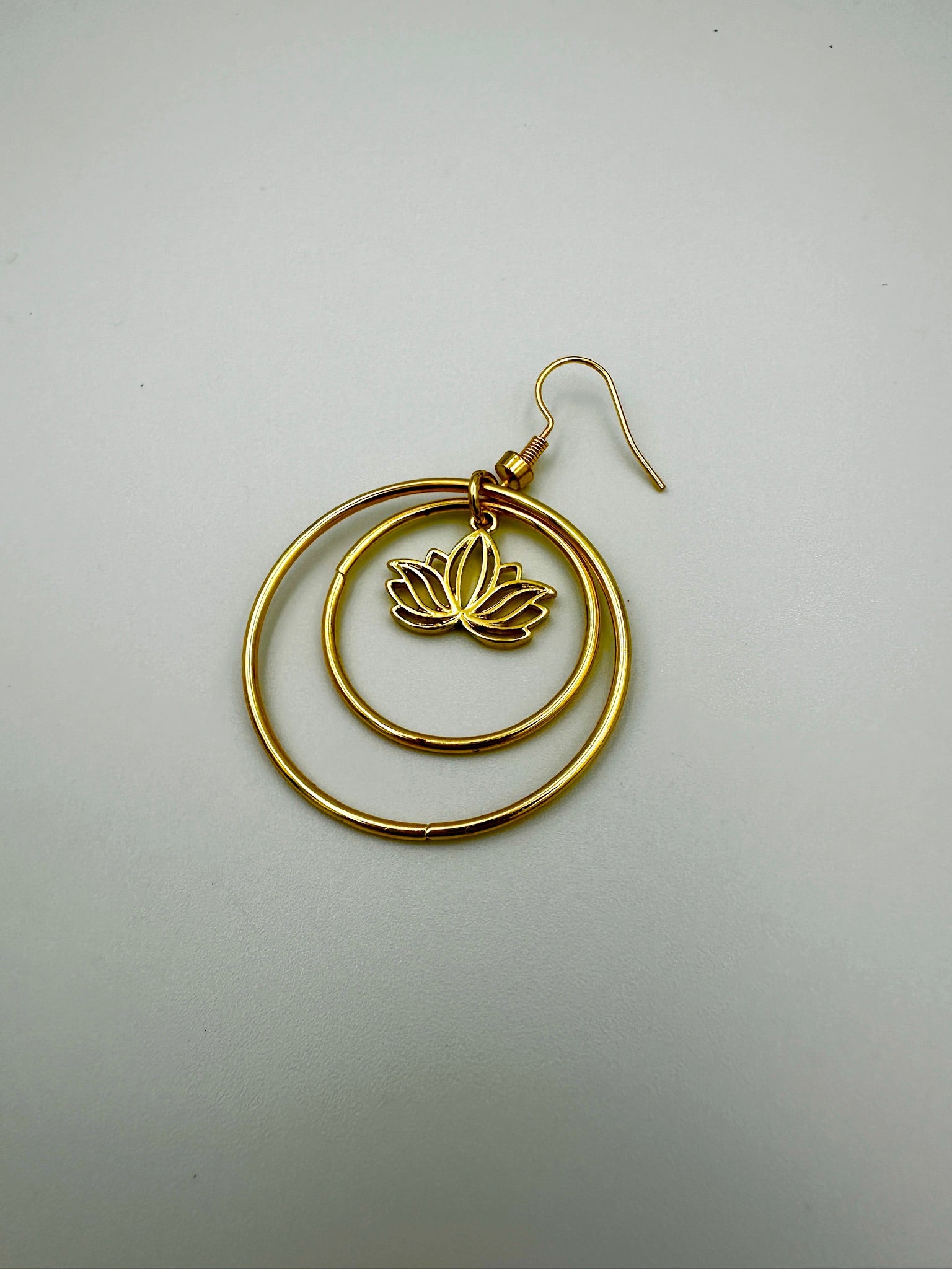 Gold hoop earring with a lotus flower design on a light gray background
