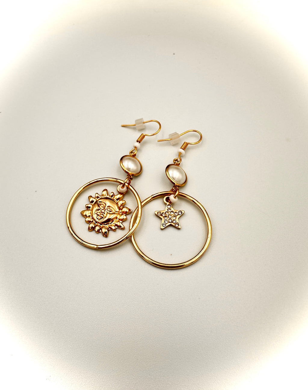 Gold hoop earrings with star and circle designs on a light background
