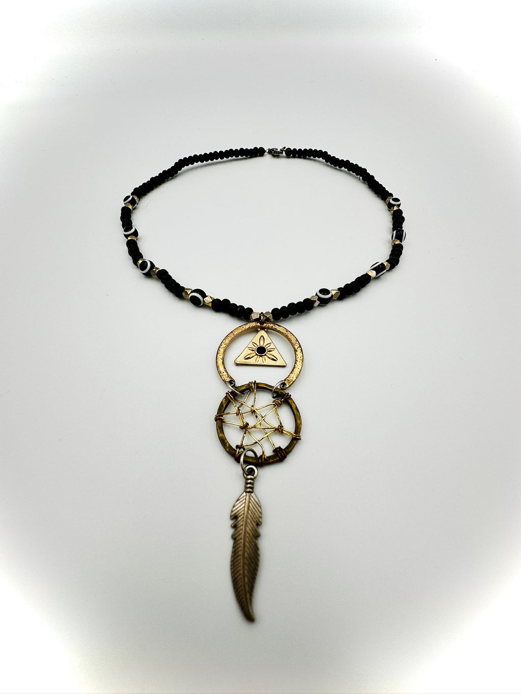 Necklace with black beaded chain, gold pendant, and feather charm on a white background
