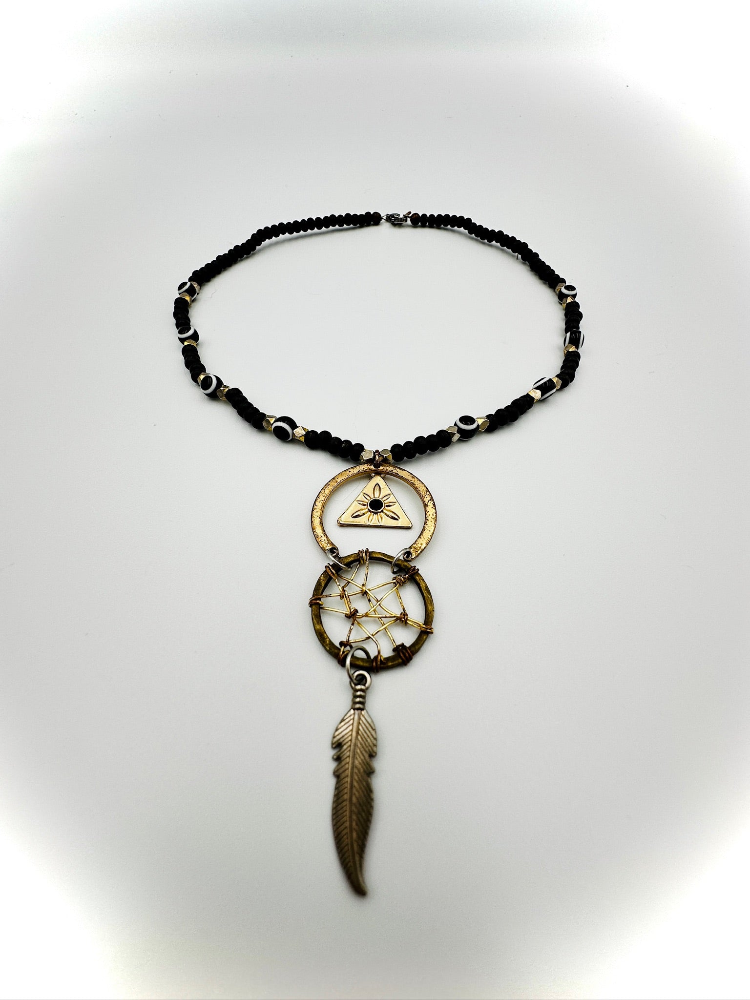 Necklace with black beaded chain, gold pendant, and feather charm on a white background
