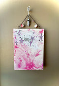 Small square canvas with star designs and text, hanging on a beige wall.