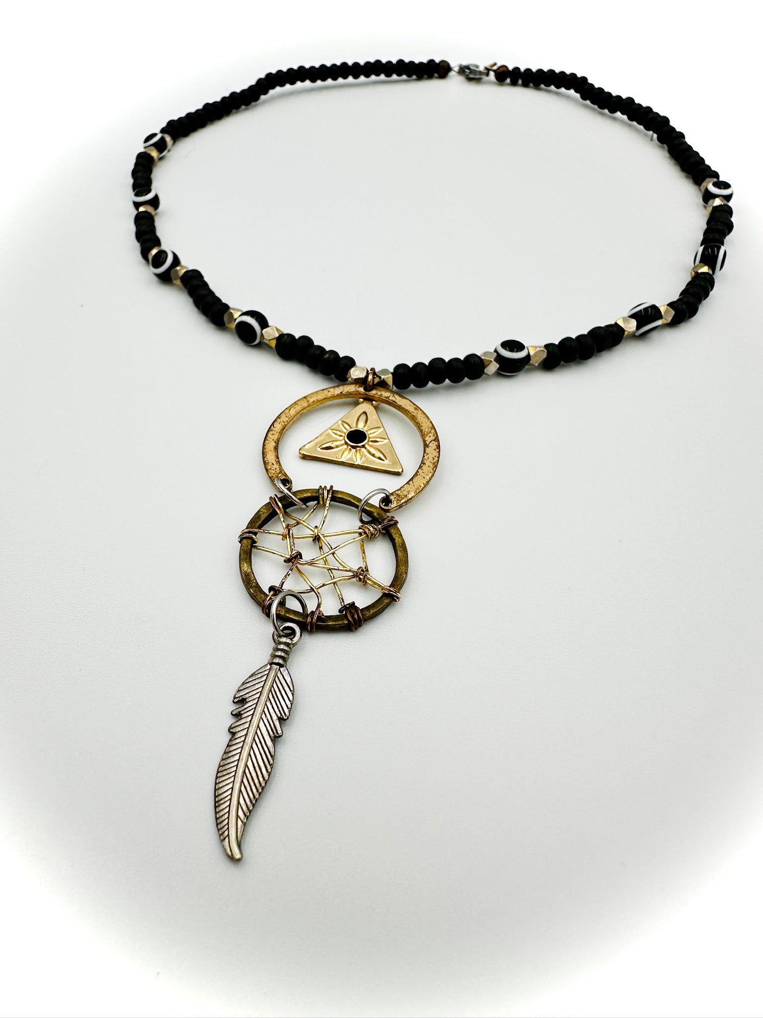 Necklace with black beads, gold pendant, and silver feather on a white background