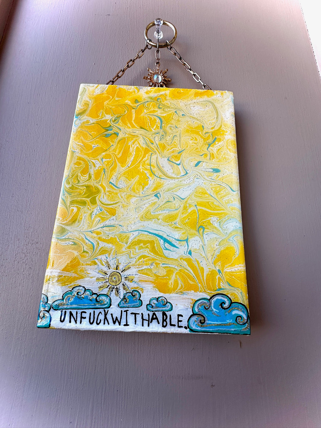 Decorative wall hanging with yellow and blue abstract design and 'UNFUCKWITHABLE' text.