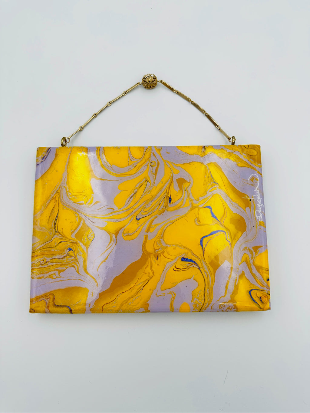 Marbled yellow and purple clutch bag with a gold strap on a white background