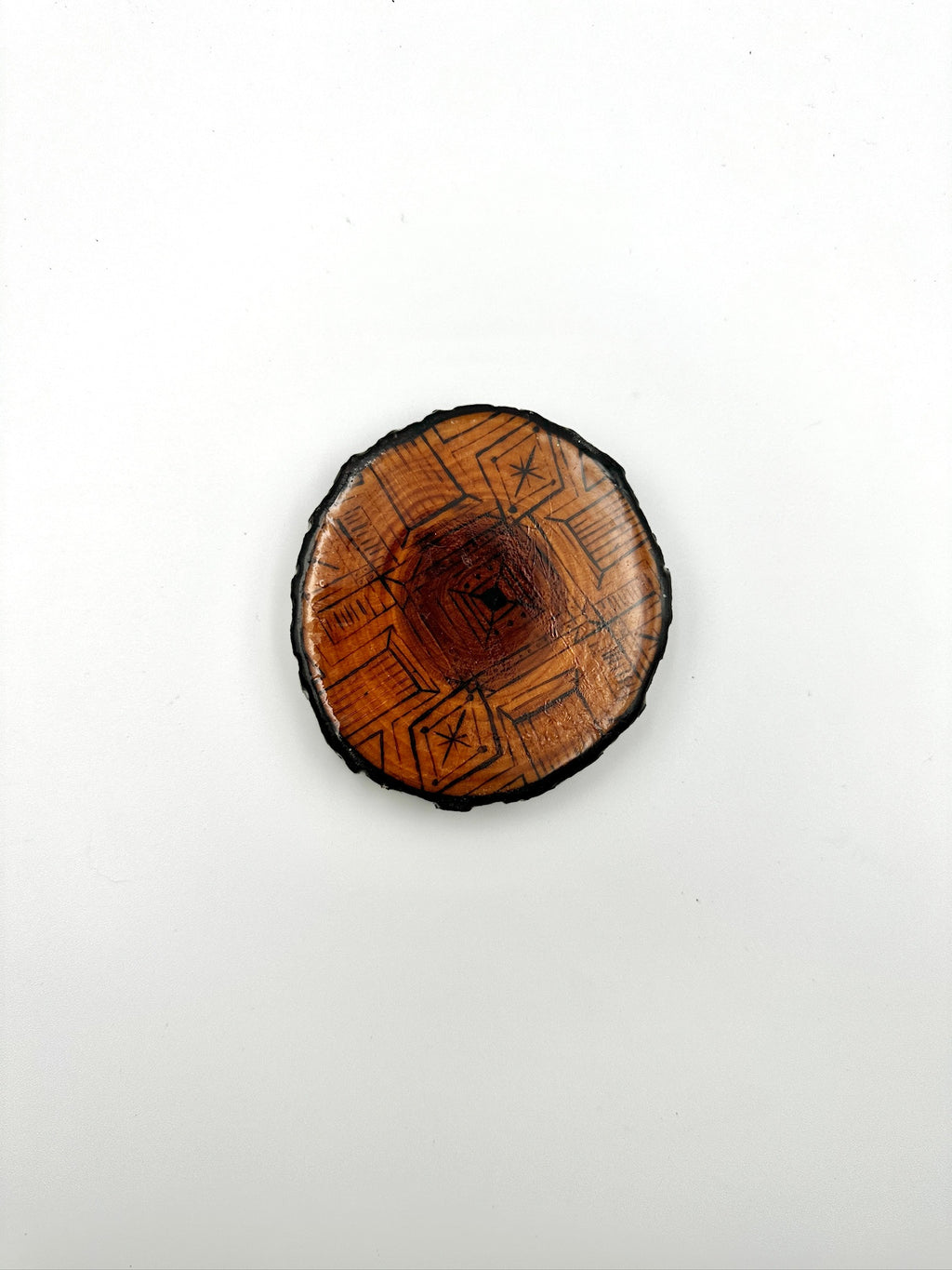 Round wooden coaster with geometric patterns on a white background