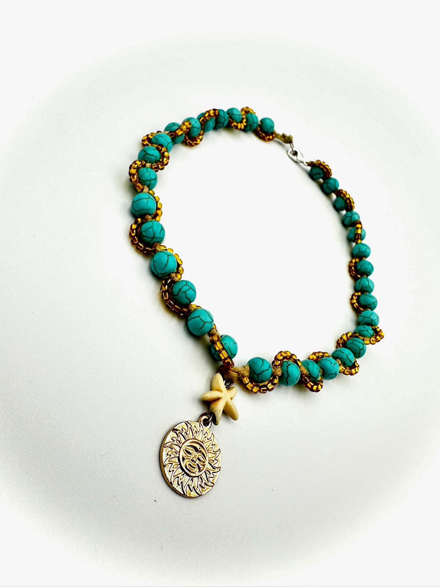 Necklace with turquoise beads and a gold charm on a white background