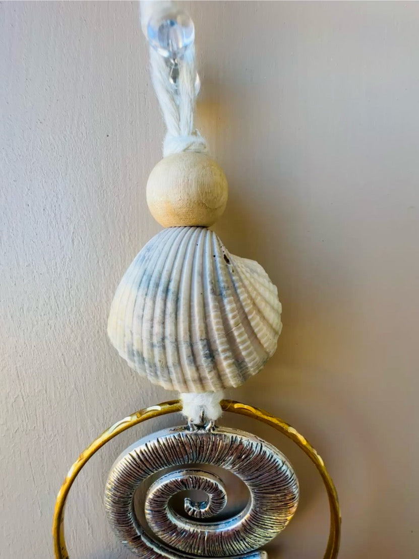Decorative wall hanging with seashells and a gold ring on a plain background