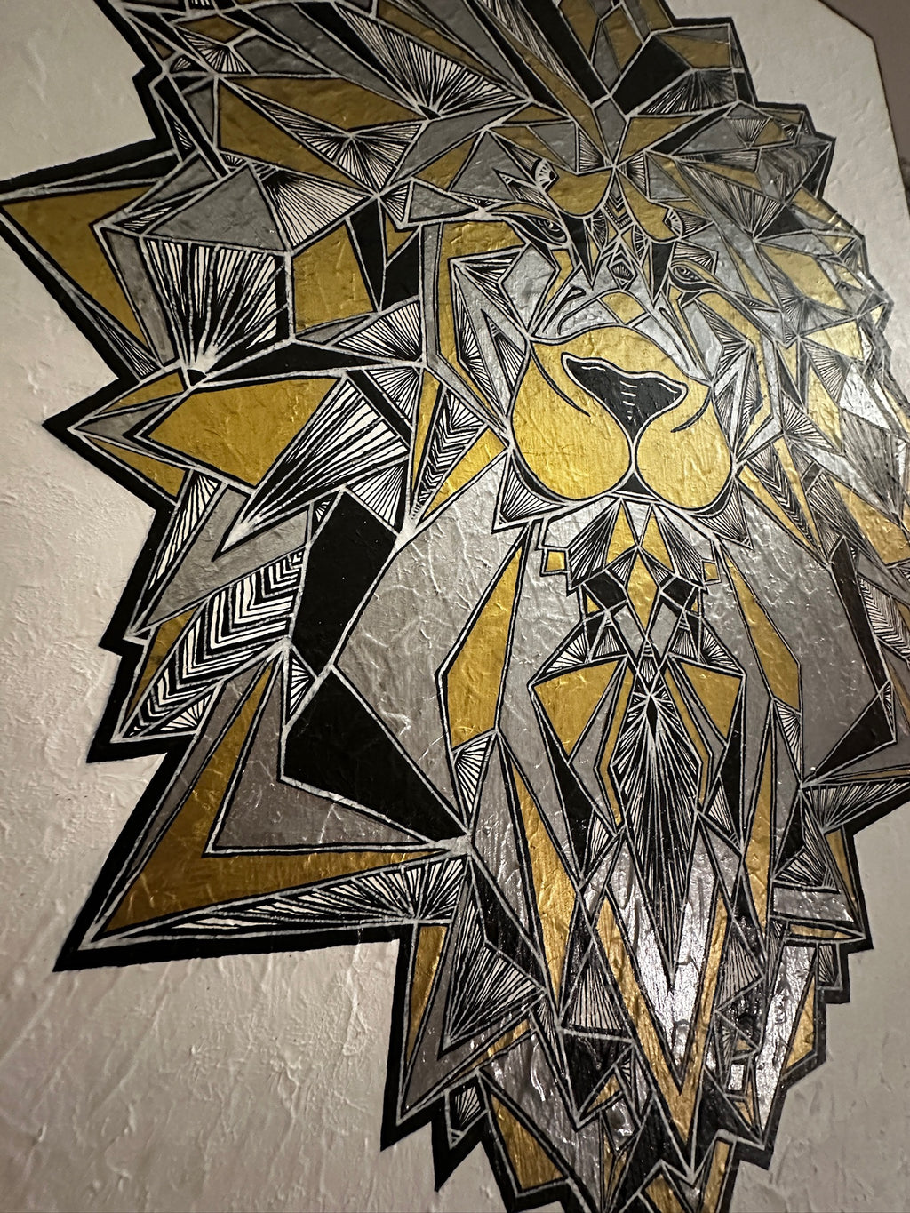Geometric lion head design in black, gold, and gray on a textured wall.