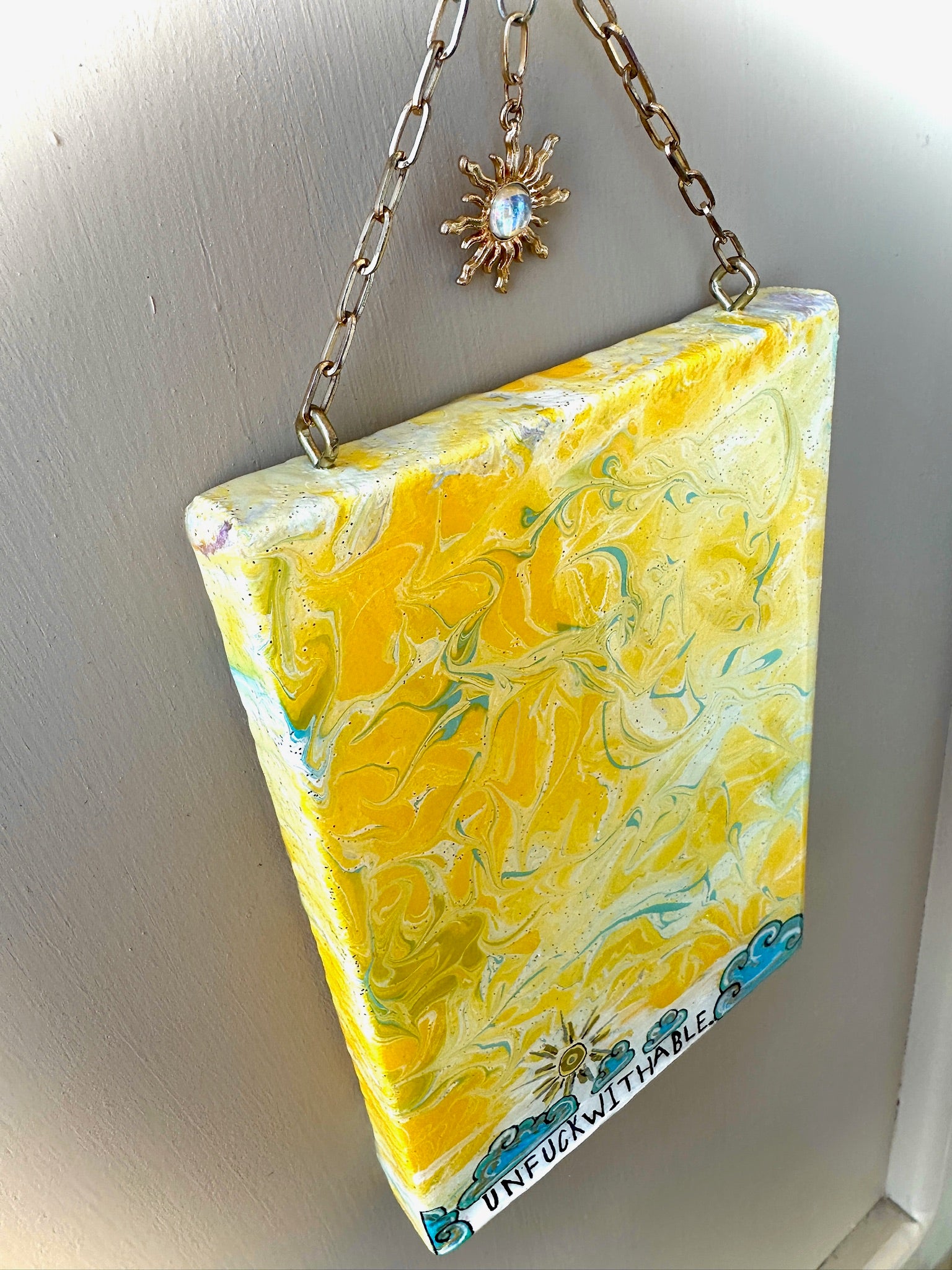 Marbled yellow and blue rectangular hanging item with a chain on a light gray background