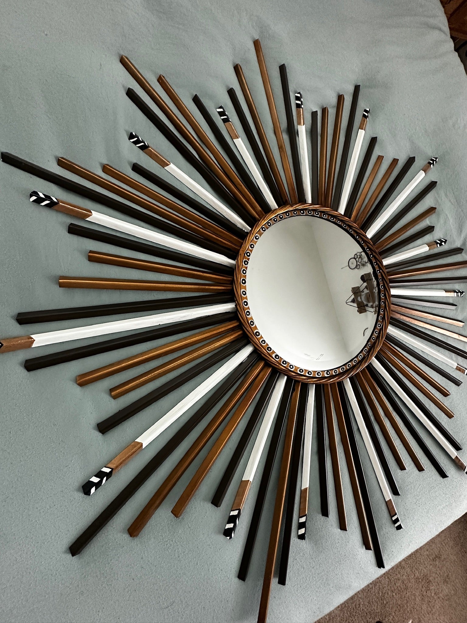 Decorative sunburst mirror with brown, black, and silver rays on a light gray wall.