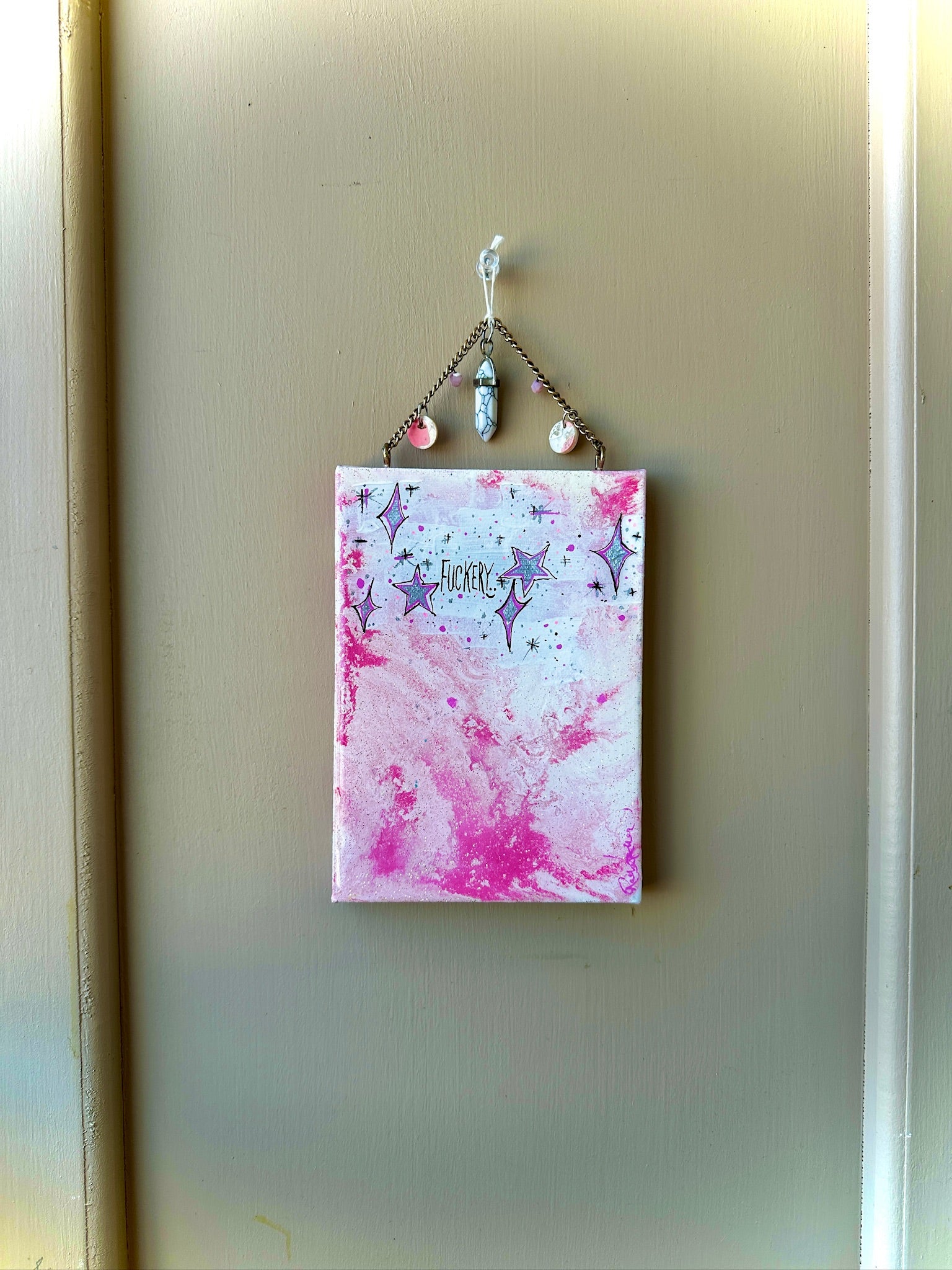 Small pink and white abstract painting with star designs hanging on a beige wall.