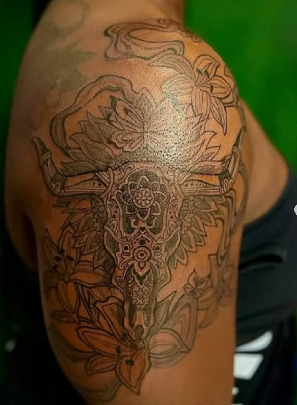 Detailed tattoo on a person's arm with floral and abstract designs against a green background